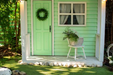 Wooden veranda with garden furniture. Modern lounge outdoors in backyard. Terrace house with plants, wooden wall and table, comfortable sofa, armchair and lanterns. Cozy space in patio or balcony. 