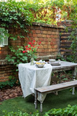 Cozy space in patio or balcony. Terrace outdoor with brick wall and plants, table and  wooden bench. Garden in summer with patio, wooden garden furniture and barbecue. Dining table in backyard at home