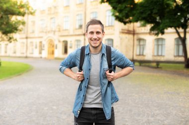 Smiling university student with backpack walking in university campus, education concept. Portrait of happy handsome man on street, copy space. man walking in the park in summer