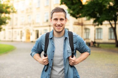 Smiling university student with backpack walking in university campus, education concept. Portrait of happy handsome man on street, copy space. man walking in the park in summer