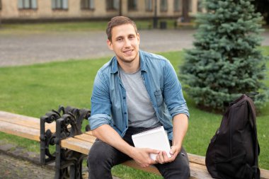 smiling man working on outdoor. education concept. Young smile man reading book while sit on bench at university campus. Happy Man study remotely. Adult student reading in park. Enjoying student life