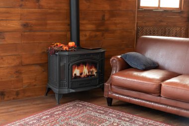 Classic black cast iron fire place with wood burning inside of it. Fragment of the interior of a country house. The iron furnace is heated. Wood burning stove, traditional heating system. 