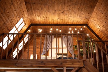 Scandinavian style interior at home. Country wooden house is spacious on two levels. Room with wooden stairway leading to second floor of modern flat. Bedroom with lamp garlands on second floor.  