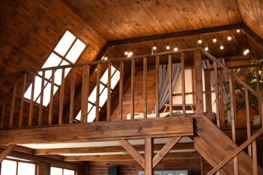 Scandinavian style interior at home. Country wooden house is spacious on two levels. Room with wooden stairway leading to second floor of modern flat. Bedroom with lamp garlands on second floor.  