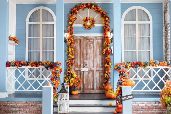 Halloween design home with yellow fall leaves and lanterns. House entrance staircase decorated for autumn holidays, fall flowers and pumpkins. Cozy wooden porch of the house with pumpkins in fall time