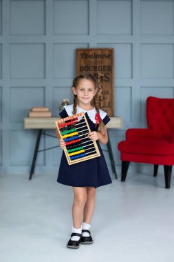 School Girl in school uniform and pigtails hair holds colorful abacus. Back to school, learning lessons. Happy smiling Little girl in dress with abacus. Kid is studying in the classroom in school 
