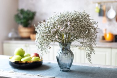 Bir kase taze elma ve mutfak tezgahında bir buket çiçekli cam vazo. Mesaj için yer var. Dekorasyonu az olan temiz bir mutfak. Evde bir buket kuru çiçek.