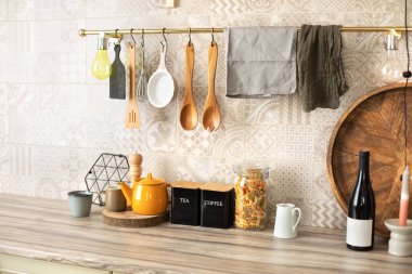 Mutfak gereçleri ve mutfak aletleri ahşap bir tezgahın üzerinde. Şık bir mutfak. Metal parmaklıklarda asılı ahşap mutfak aletleri. Seramik tabaklar, tabaklar ve sofrada rahat bir dekor