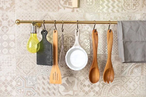 Wooden kitchen utensils hanging on metal railing. Kitchen spatulas hand on railing on a tiled wall with geometric pattern in kitchen in Scandinavian style. Kitchenware object and interior photo.