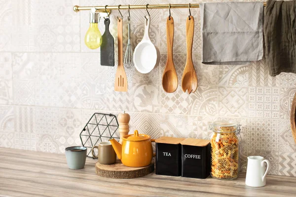 Kitchen utensils and utensils on a wooden countertop. Stylish kitchen interior. Wooden kitchen utensils hanging on metal railing. Ceramic plates, dishes and cozy decor on table