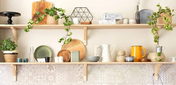 Kitchen wooden shelves with various ceramic jars and cookware. Open shelves in the kitchen. Stylish scandi cuisine interior decor. Ceramic plates, dishes, utensils and cozy decor on wooden shelfs.