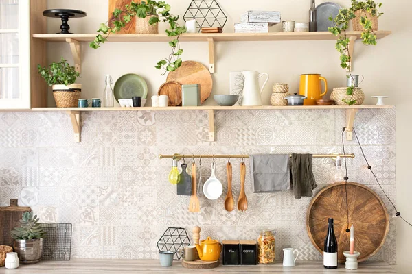 Ceramic plates, dishes, utensils and cozy decor on wooden shelfs. Kitchen wooden shelves with various ceramic jars and cookware. Open shelves in the kitchen. Stylish scandi cuisine interior decor.