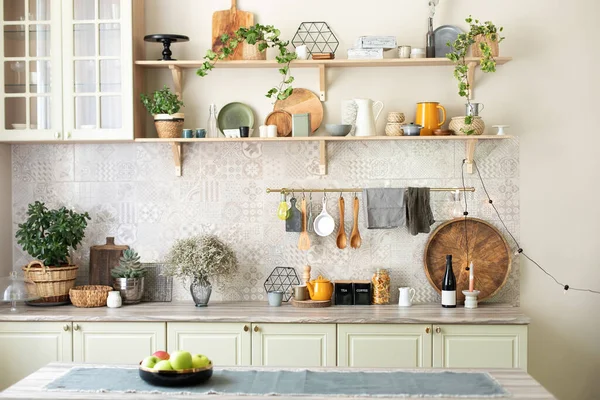 Modern home decor. Kitchen utensils, dishes and plates. Kitchen island in dining room. Green wooden kitchen interior with wooden shelf and cozy decoration. Stylish cuisine with flowers in vase.