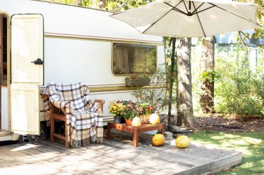 Ekose ve masalı koltuklu rahat bir karavan evi. Bahçedeki kamp alanında. Çiçek saksısı ve balkabaklarıyla dolu bir kamp alanı. Cadılar Bayramı için dekore edilmiş verandanın yanındaki tahta sandalye.