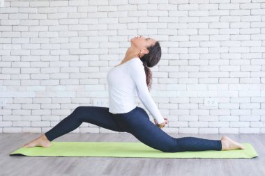 Beyaz tuğlalı minder üzerinde yoga yapan güzel Latin bir kadın. Evde sağlıklı kadın aktivitesi.