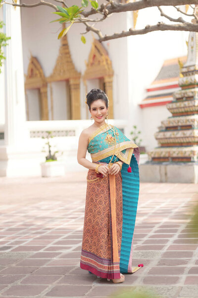 Portrait Asian women smiling and wearing Thai national costumes are inside temples to worship Buddha with flower garlands on important religious days for Thai people.