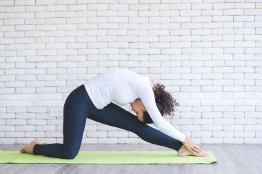Beyaz tuğlalı minder üzerinde yoga yapan güzel Latin bir kadın. Evde sağlıklı kadın aktivitesi.