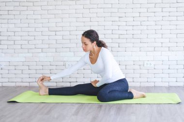 Beyaz tuğlalı minder üzerinde yoga yapan güzel Latin bir kadın. Evde sağlıklı kadın aktivitesi.