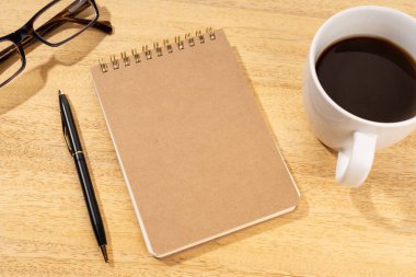 Tahta masanın üzerinde boş bir karton not defteri, bir fincan kahve ve gözlüklü. Şablon maketi