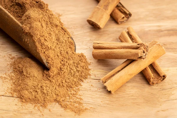 stock image Cinnamon powder and cinnamon sticks in wooden scoop on wooden table. Close up