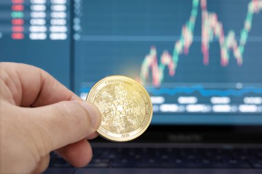 Arka planda dizüstü bilgisayarda bir Cardano madeni para ve çizelgesi tutuyor. Kripto para birimi ticareti veya yatırım kavramı