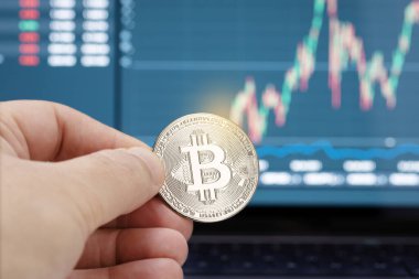 Arka planda dizüstü bilgisayar ekranında bir bitcoin para ve çizelge tutuyor. Kripto para birimi ticareti veya yatırım kavramı