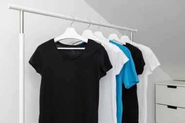 Beyaz askılarda asılı çeşitli tişörtlerden oluşan bir grup. Giysi rafı. Şablon, modelle.
