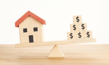 Ev ya da Emlak Yatırım Konsepti. Ev modeli ve tahtadan bloklar, tahterevallinin üzerinde dolar işareti dengeleniyor.