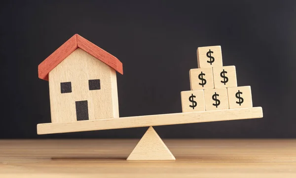 House or Property investment concept. House model and wooden blocks with dollar sign balancing on a seesaw