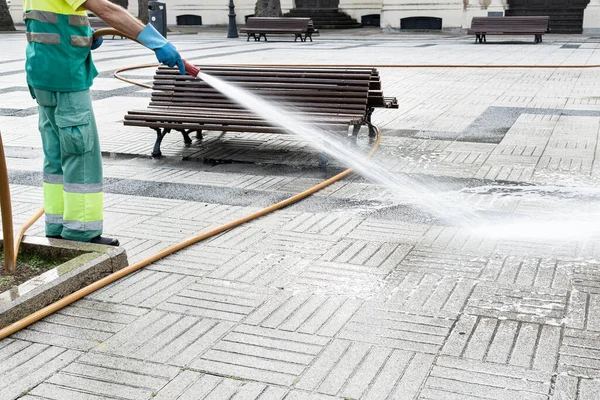 Sweeper cleaning a public park with water using a hosepipe. Public maintenance concept. Copy space