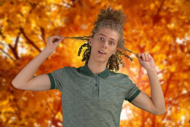 Parktaki genç bir adamın sonbahar fotoğrafı. Sıcak renklerde fotoğraf. Sarı yaprakların arka planına karşı. Sonbahar renkleri