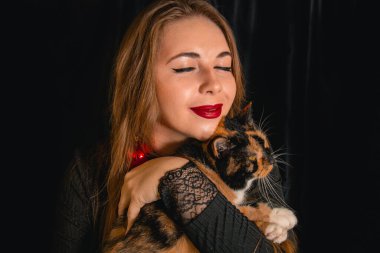 Siyah arka planda kedisi olan güzel bir sarışın. Hayvanların ve insanların arkadaşlığı kavramı.