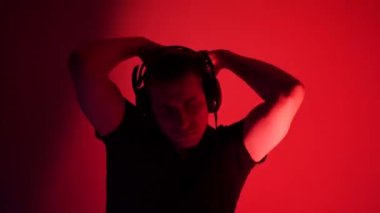 Handsome man listening to music using headphones in colorful neon light. The student is resting after work and enjoying music. Dance with fluid hand movements to the rhythm