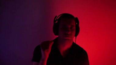 Excited young man in headphones is dancing in the club. Modern rave. Dance with fluid hand movements to the rhythm. Music lover