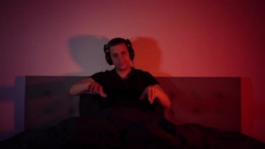 Handsome man listening to music using headphones in colorful neon light. The student is resting after work and enjoying music. Dance with fluid hand movements to the rhythm