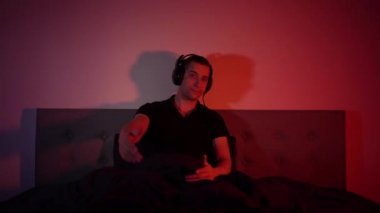 Handsome man listening to music using headphones in colorful neon light. The student is resting after work and enjoying music. Dance with fluid hand movements to the rhythm