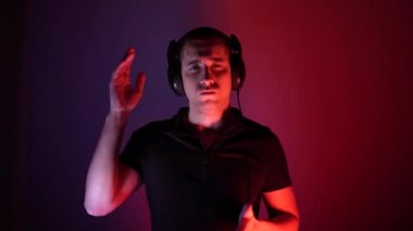 Attractive dancing man. Portrait in neon light. Smiling guy with big headphones, moving to the rhythm of the sound on the blue-red colored glow of copy space. Music lover. Stereo technology