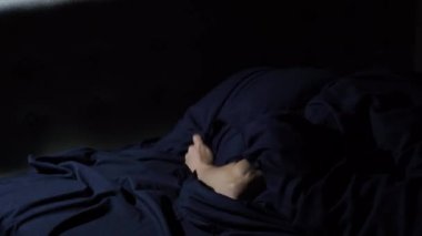 Huzursuz uyku. Genç adam yatakta bir o yana bir bu yana dönüyor. Gürültüyü duymamak için başını yastıkla örtüyor..