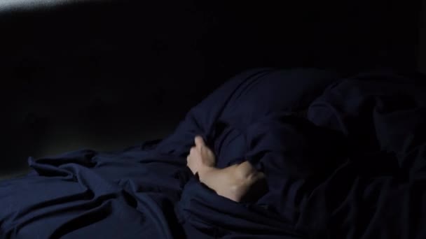 Schlafstörungen. Der junge Mann wirft und dreht sich im Bett. Bedeckt seinen Kopf mit einem Kissen, um den Lärm nicht zu hören. — Stockvideo