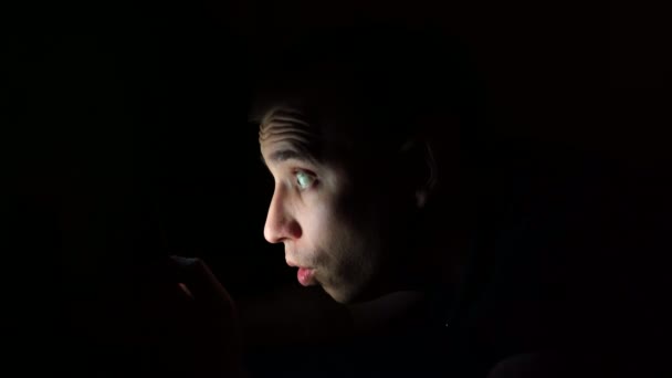 Giovane ragazzo guarda il telefono prima di andare a letto di notte con una faccia sorpresa. Esamina le informazioni al telefono. — Video Stock
