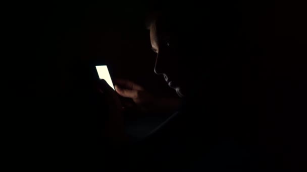 Giovane ragazzo guarda il telefono prima di andare a letto la notte. Esamina le informazioni al telefono. — Video Stock
