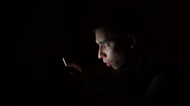 Молодий хлопець дивиться на телефон перед сном вночі з здивованим обличчям. Досліджує інформацію по телефону . — стокове відео