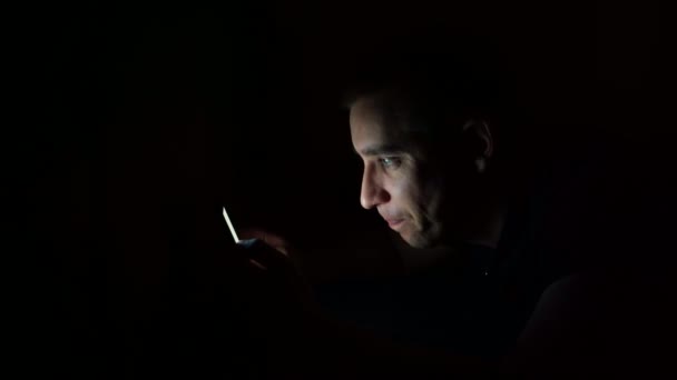 Young guy looks at the phone before going to bed at night. Examines information on the phone. — Stock Video
