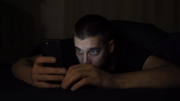 Een jongeman kijkt naar de telefoon voordat hij 's nachts naar bed gaat en valt in slaap. Onderzoekt informatie over de telefoon. — Stockvideo