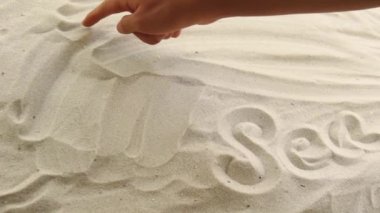 hand draws the inscription White Sea on the sand. Sunny coast of the sea and ocean. Symbol of rest and vacations at the resort