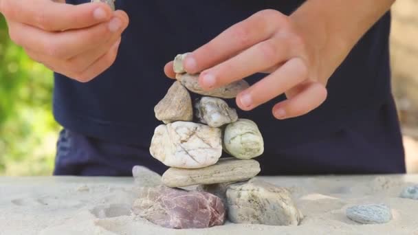Man builds a pyramid of sea stones. heap of smooth pebbles. zen stones close-up. the concept of peace of mind and relaxation in the resort — ストック動画