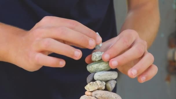 Člověk staví pyramidu z mořských kamenů. hromada hladkých oblázků. Zenové kameny zblízka. koncept klidu mysli a relaxace v resortu — Stock video