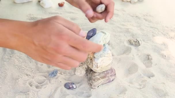 O homem constrói uma pirâmide de pedras marinhas. monte de seixos lisos. Pedras zen close-up. o conceito de paz de espírito e relaxamento no resort — Vídeo de Stock