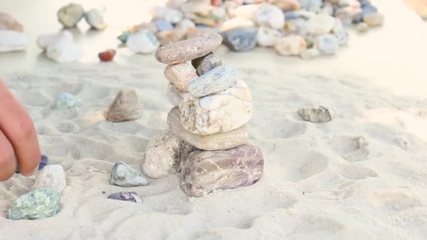 El hombre construye una pirámide de piedras marinas. montón de guijarros suaves. Piedras zen de cerca. el concepto de paz mental y relajación en el resort — Vídeo de stock