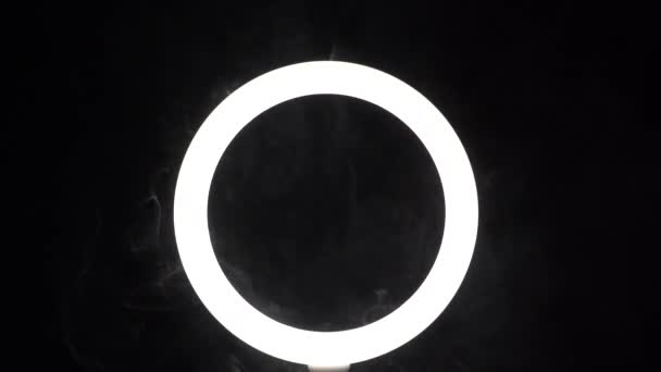 A stream of smoke in front of a ring of light from a led lamp on a black background close-up. The vaper blows steam in the frame. The concept of a dance club and a stage with spotlights — Video